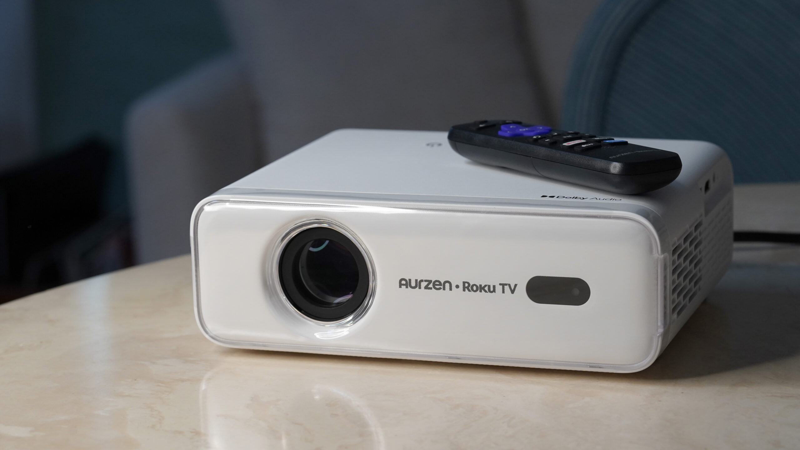An Aurzen Roku TV EAZZE D1R projector rests on a marble surface with its included remote.