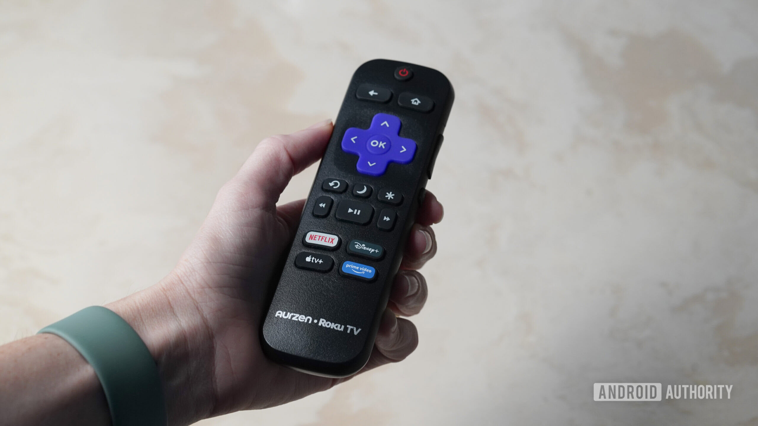 A user holds the remote that ships with the Aurzen Roku TV EAZZE D1R.