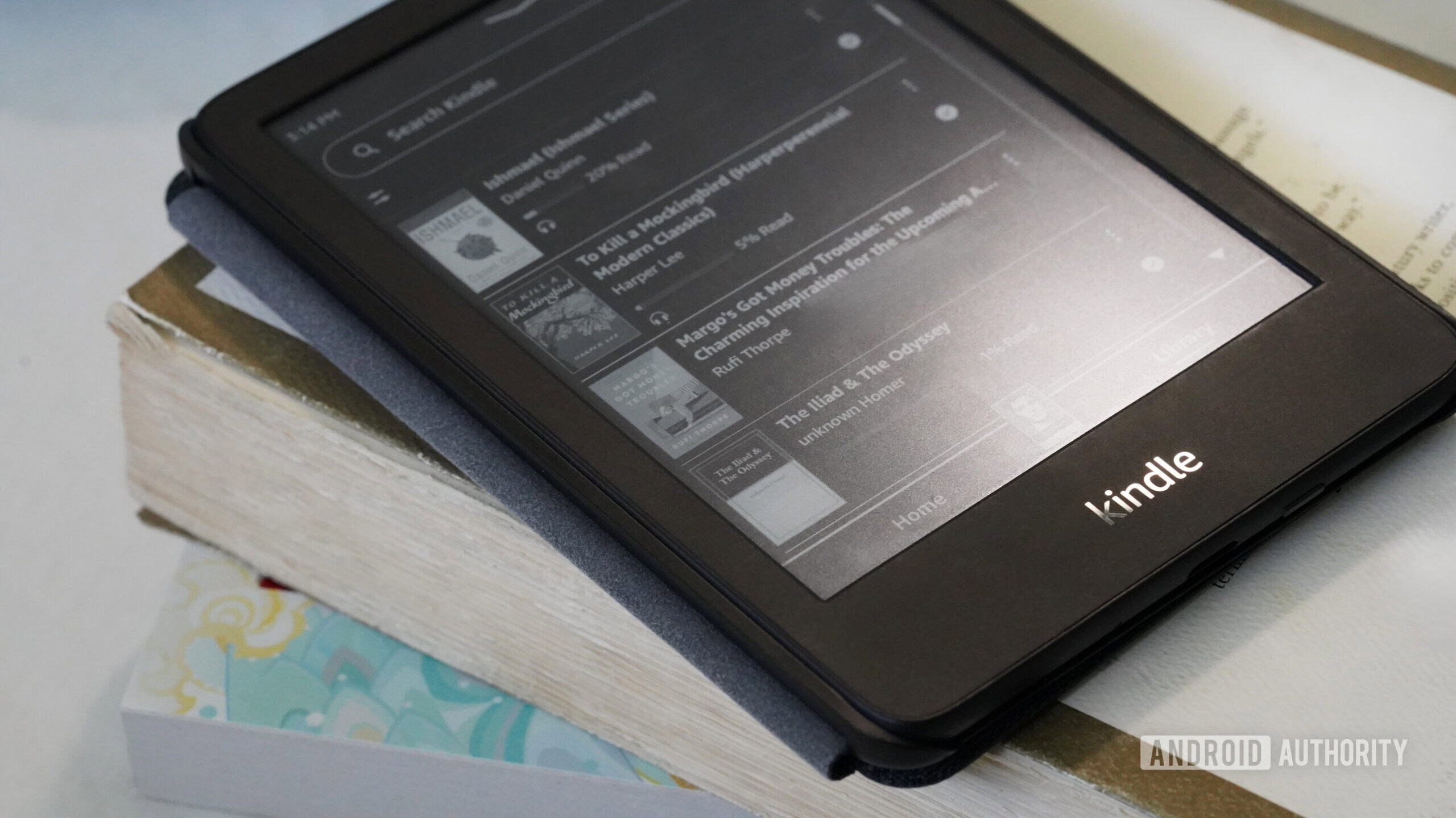 A Kindle rests on a short stack of paperback books.