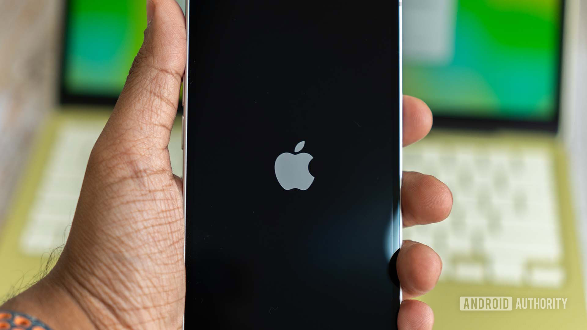 Apple iPhone 17e showing Apple logo on display during boot, with MacBook Neo in the background
