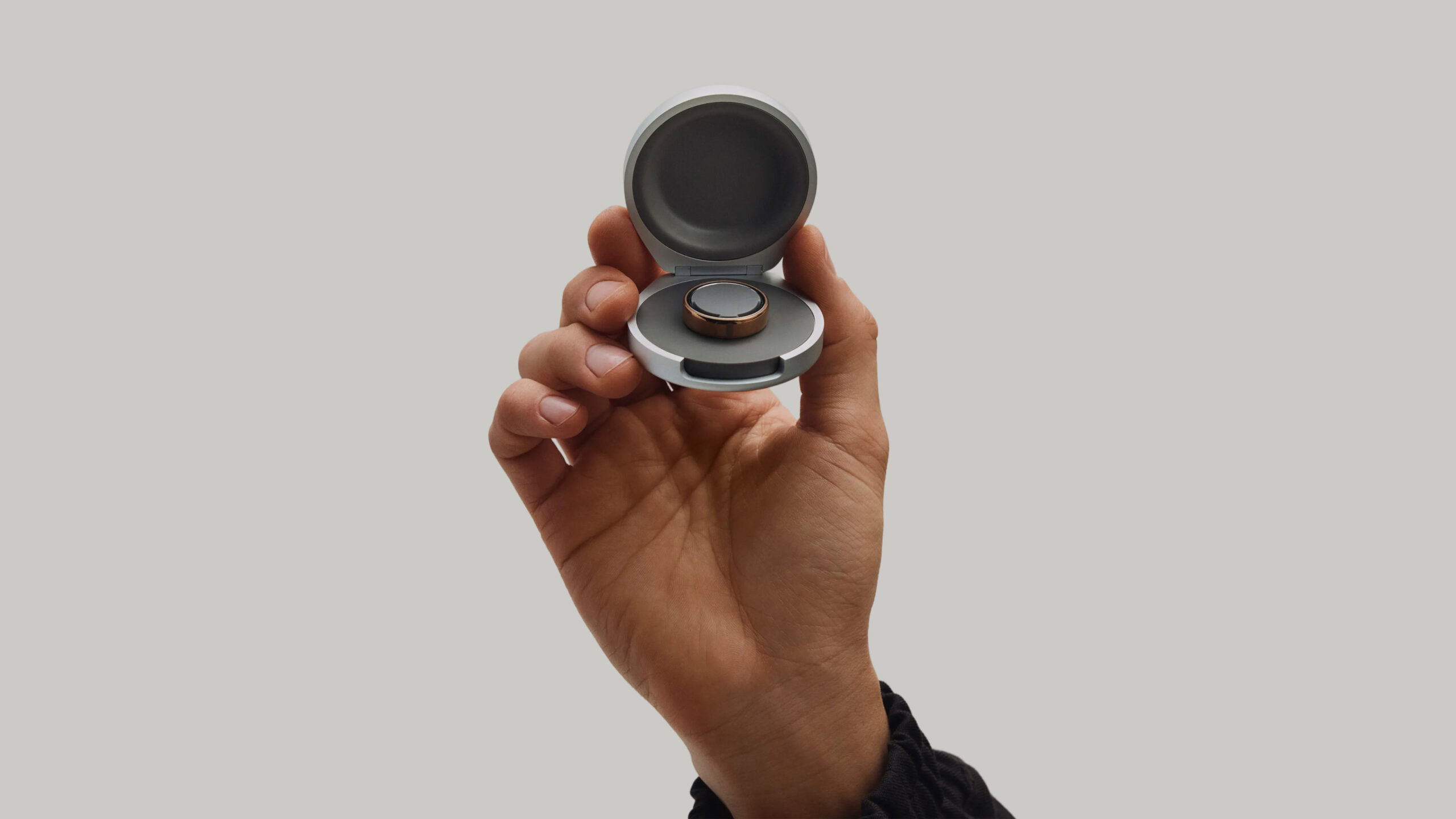 A user holds an Oura Ring 5 Charging Case with a Ring 5 inside. 