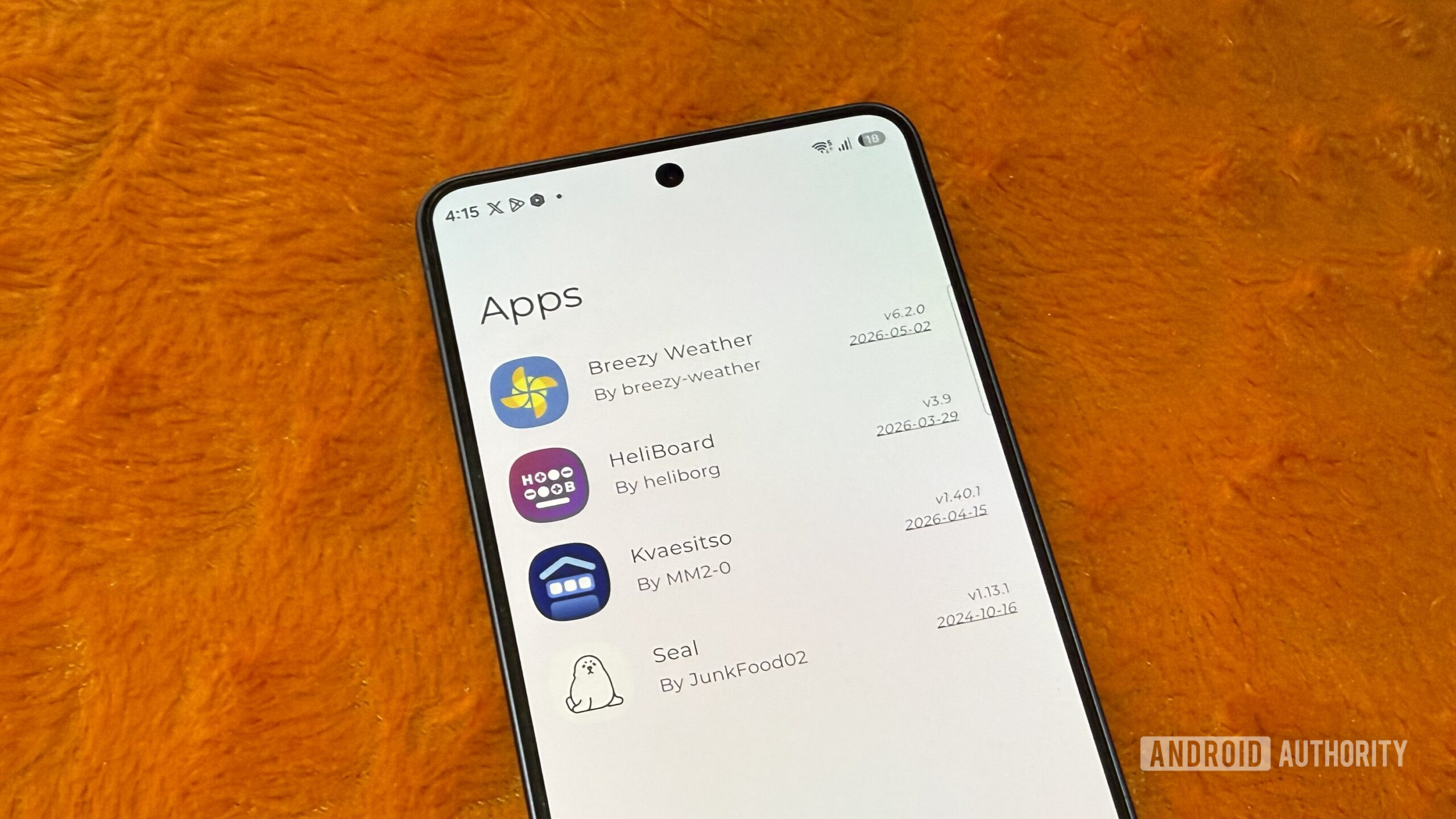 Samsung phone on an orange pillow showing a list of apps