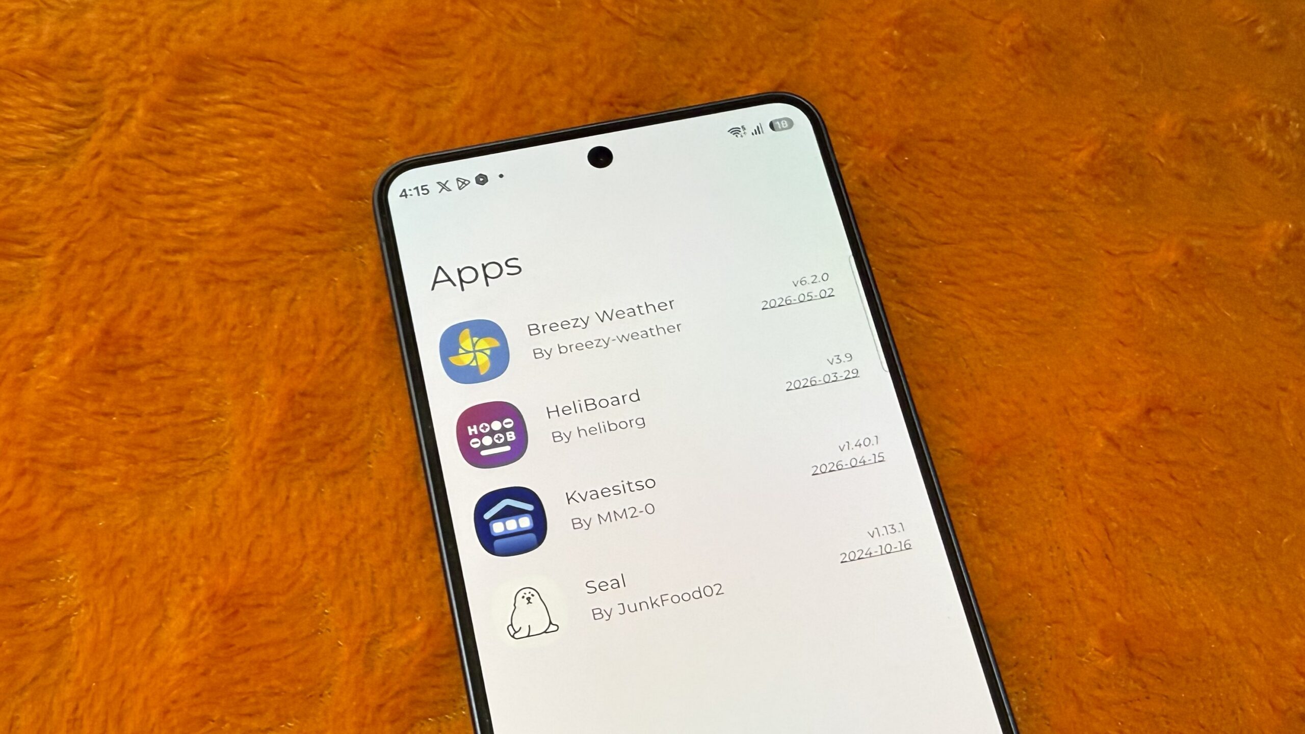 Galaxy phone on an orange pillow showing a list of apps