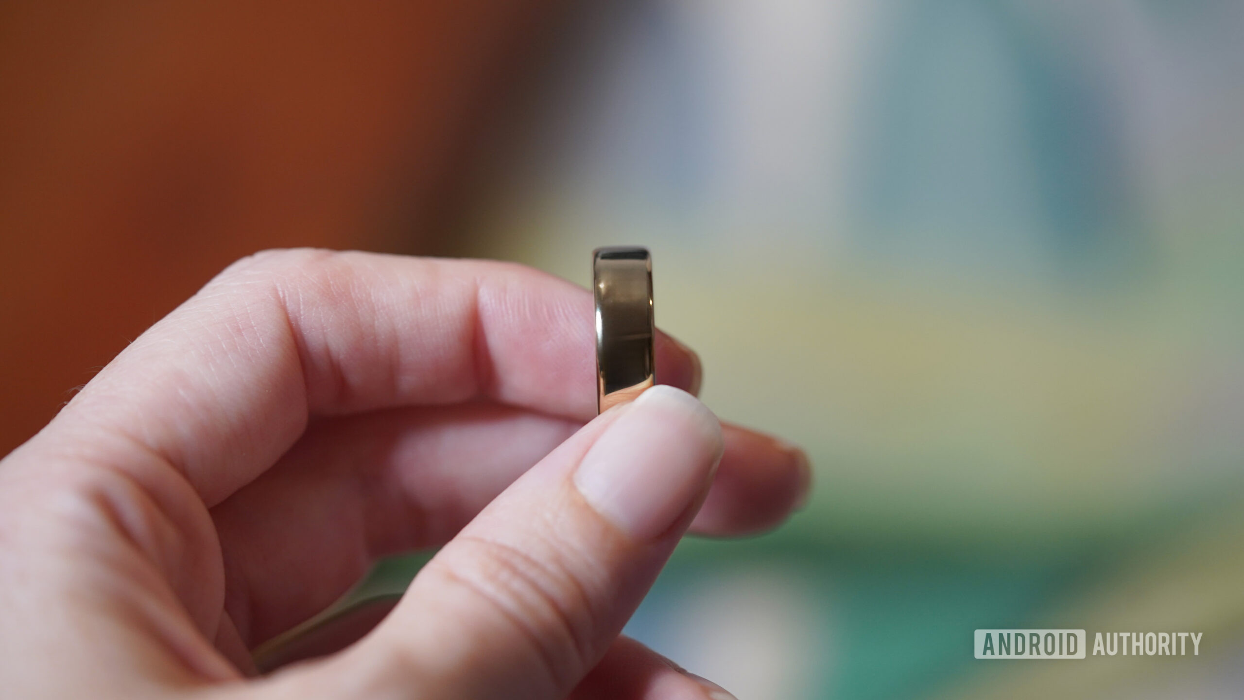 A user holds a Gold Oura Ring 5 between their fingers.