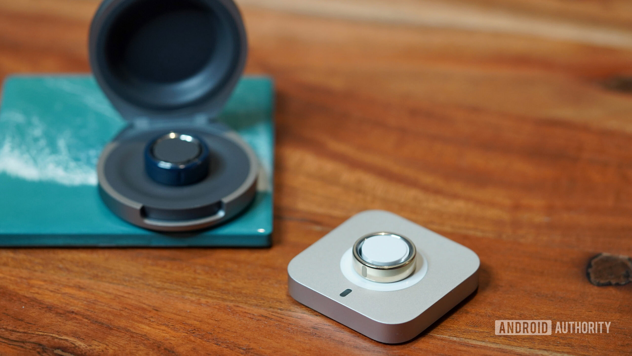 An Oura Ring 5 on its charger rests in front of an Oura Ring 4 in its charging case.