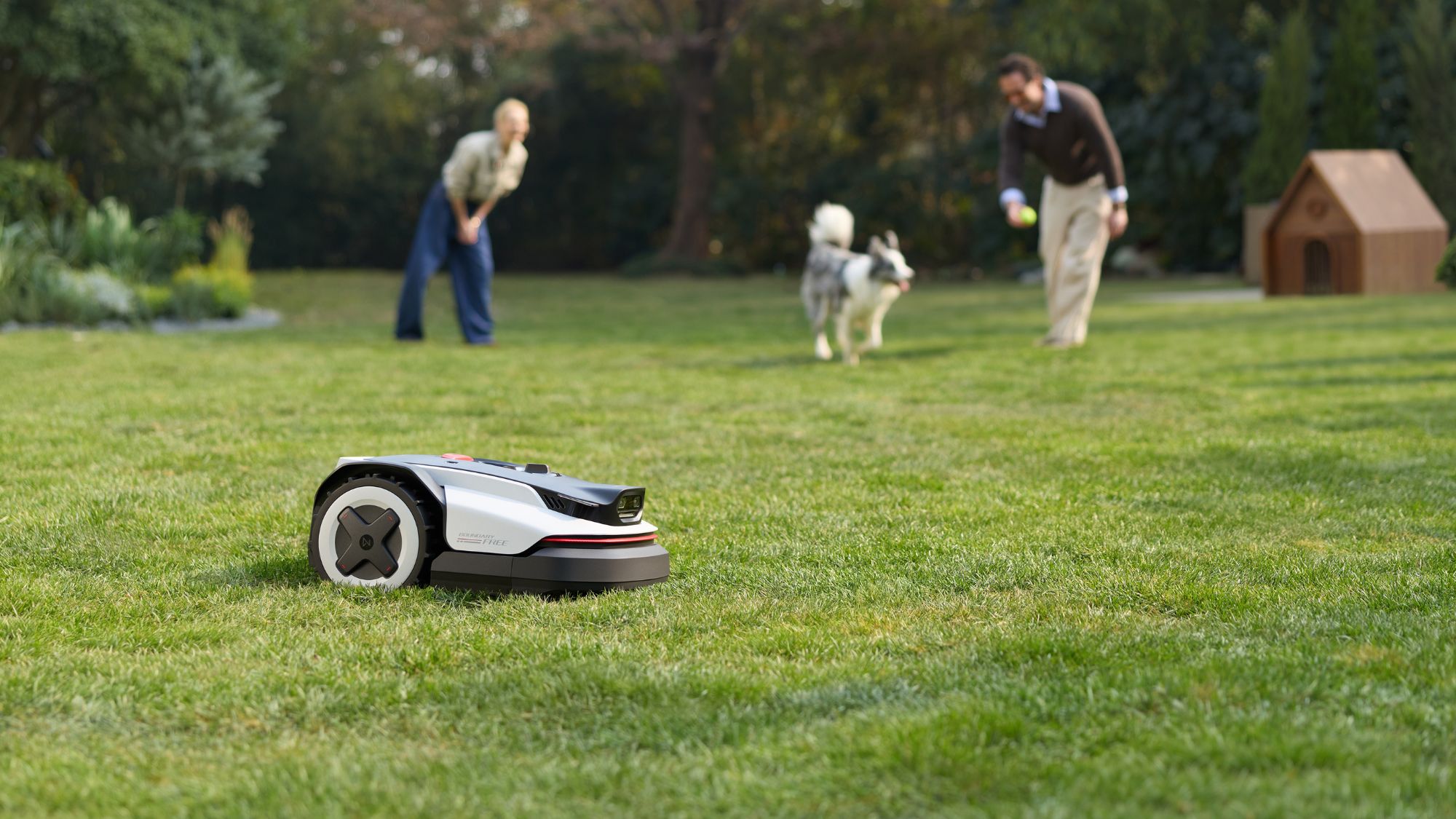 RockNeo Q110H robotic lawnmower near a dog and two adults RockNeo Q110H robotic lawnmower near a dog and two adults