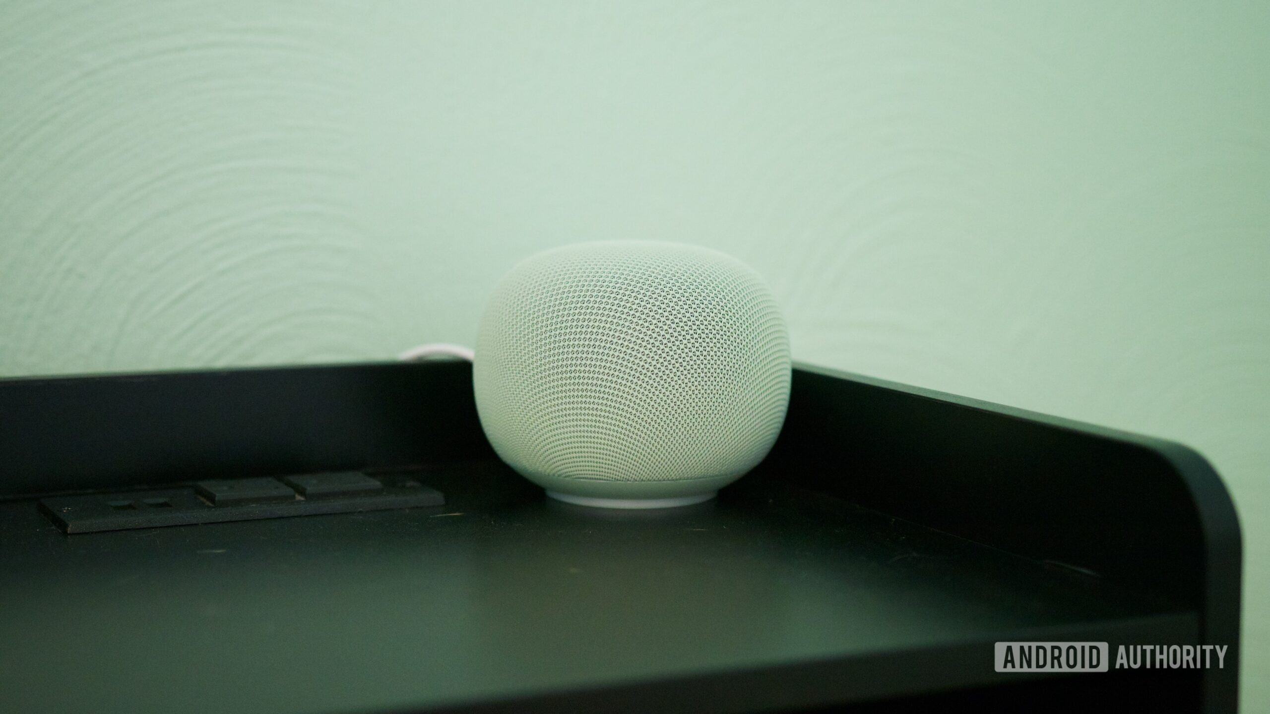 The Google Home Speaker sitting on a black nightstand.