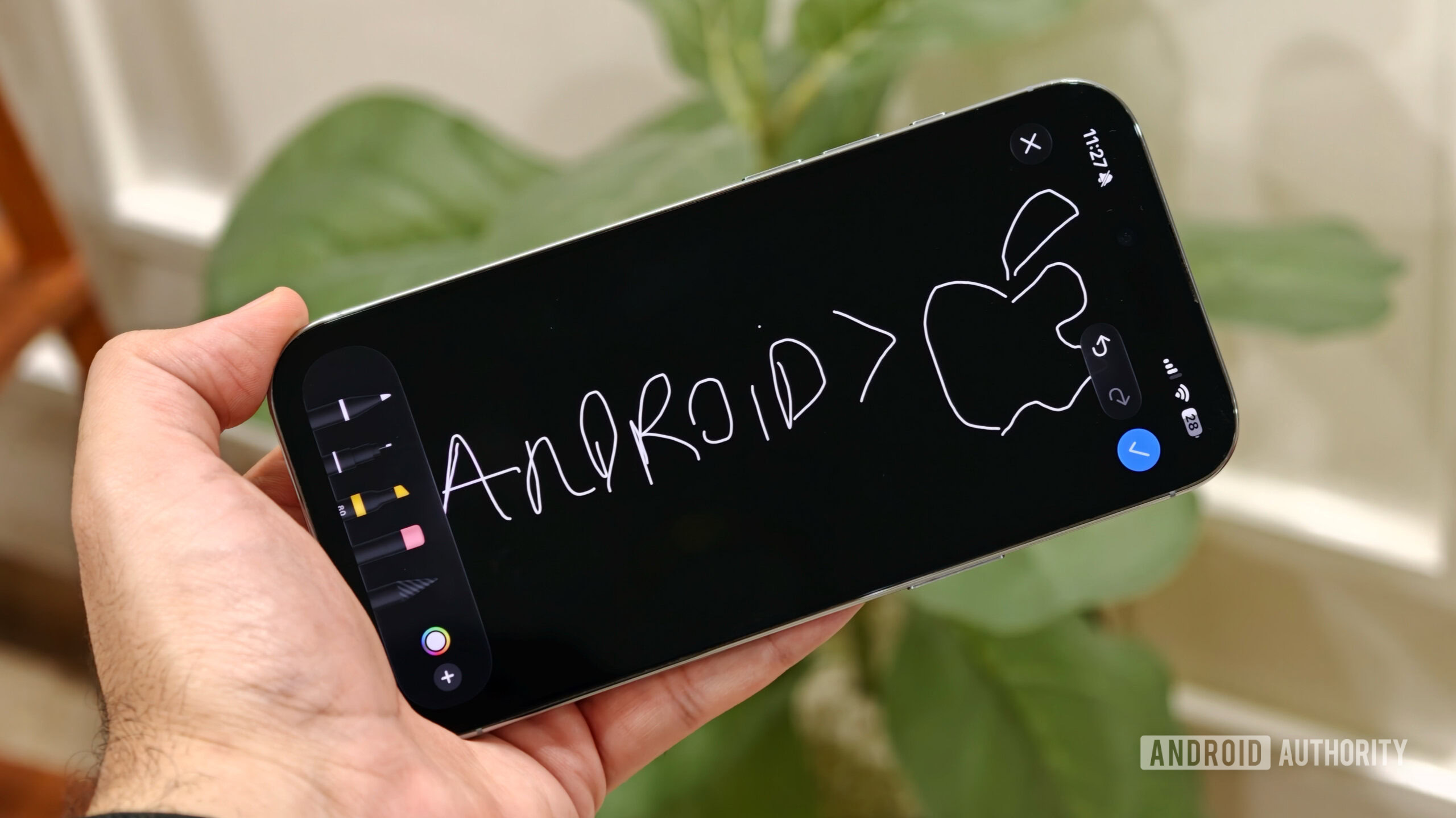 ios messages drawing feature A hand holding an iPhone in landscape mode displaying a handwritten drawing on a dark canvas inside the Messages app