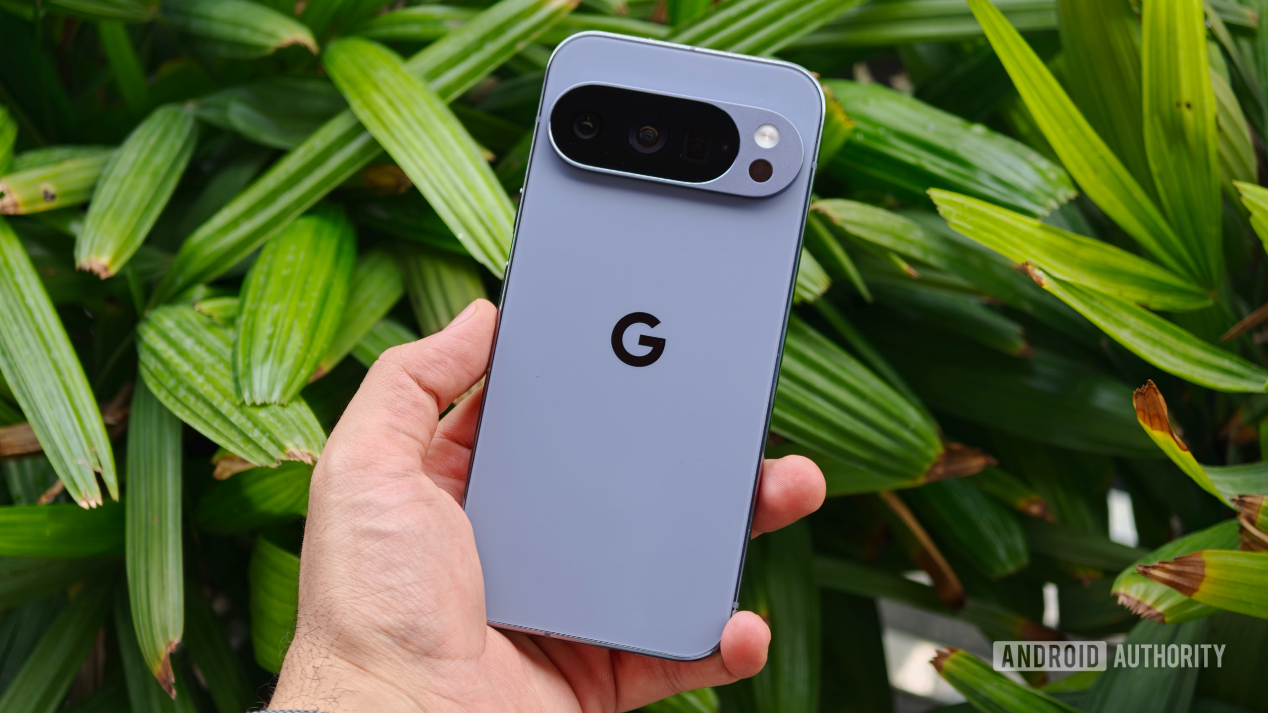 pixel 10 pro hand green 1 A hand holding the Google Pixel 10 Pro, showcasing the prominent horizontal camera visor against a lush green leafy background
