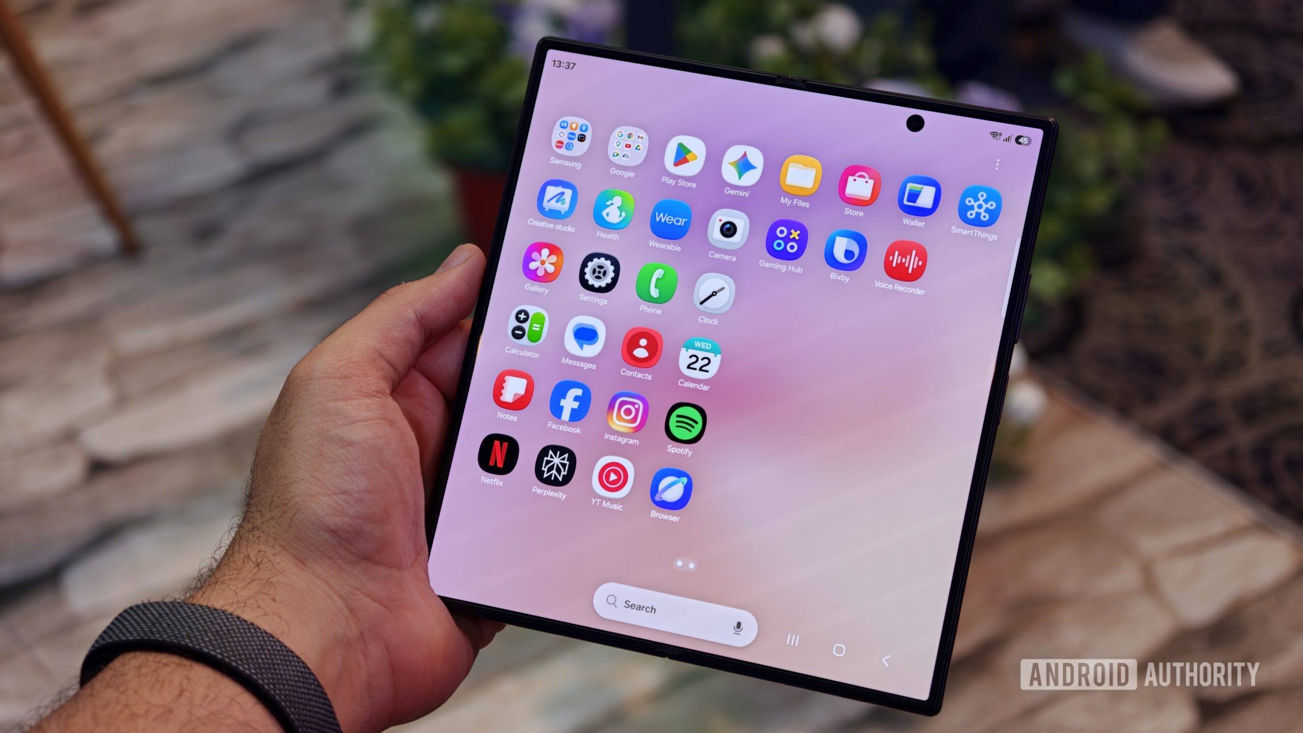 A person holding the unfolded Samsung Galaxy Z Fold 8 Ultra showing the full app drawer screen grid on its large main display
