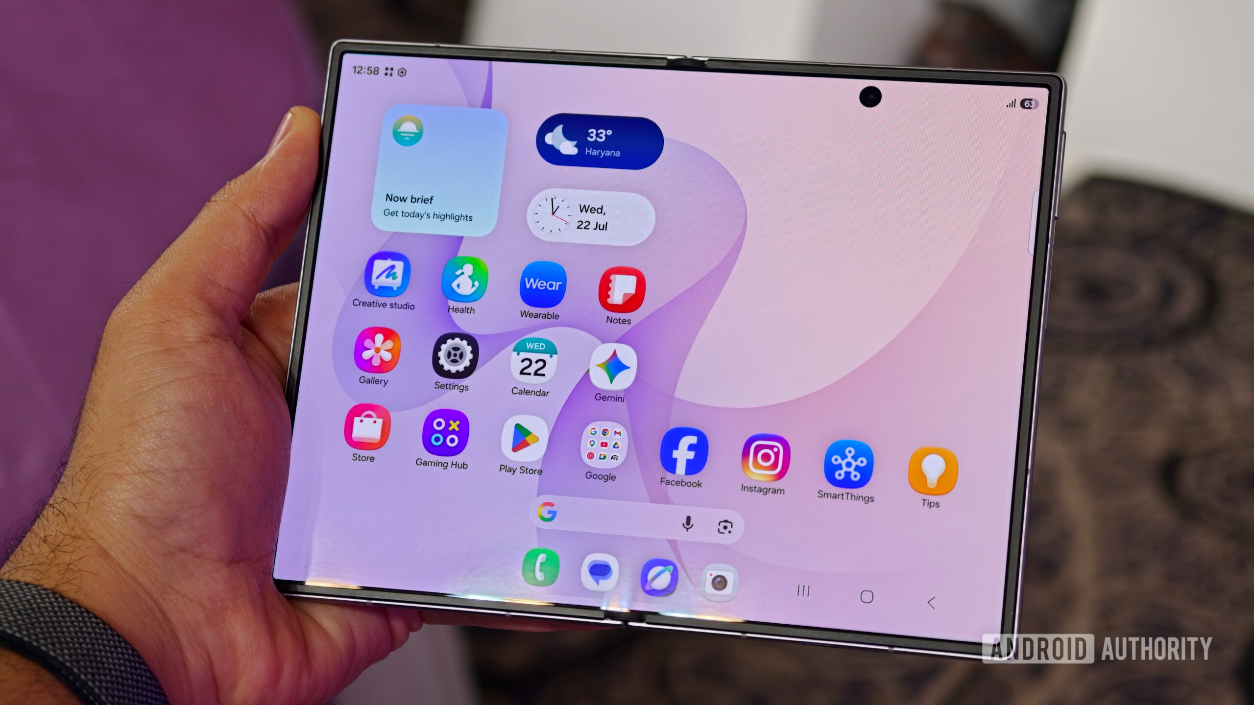 A person holding the unfolded Samsung Galaxy Z Fold 8 displaying the One UI home screen with weather widgets and app icons