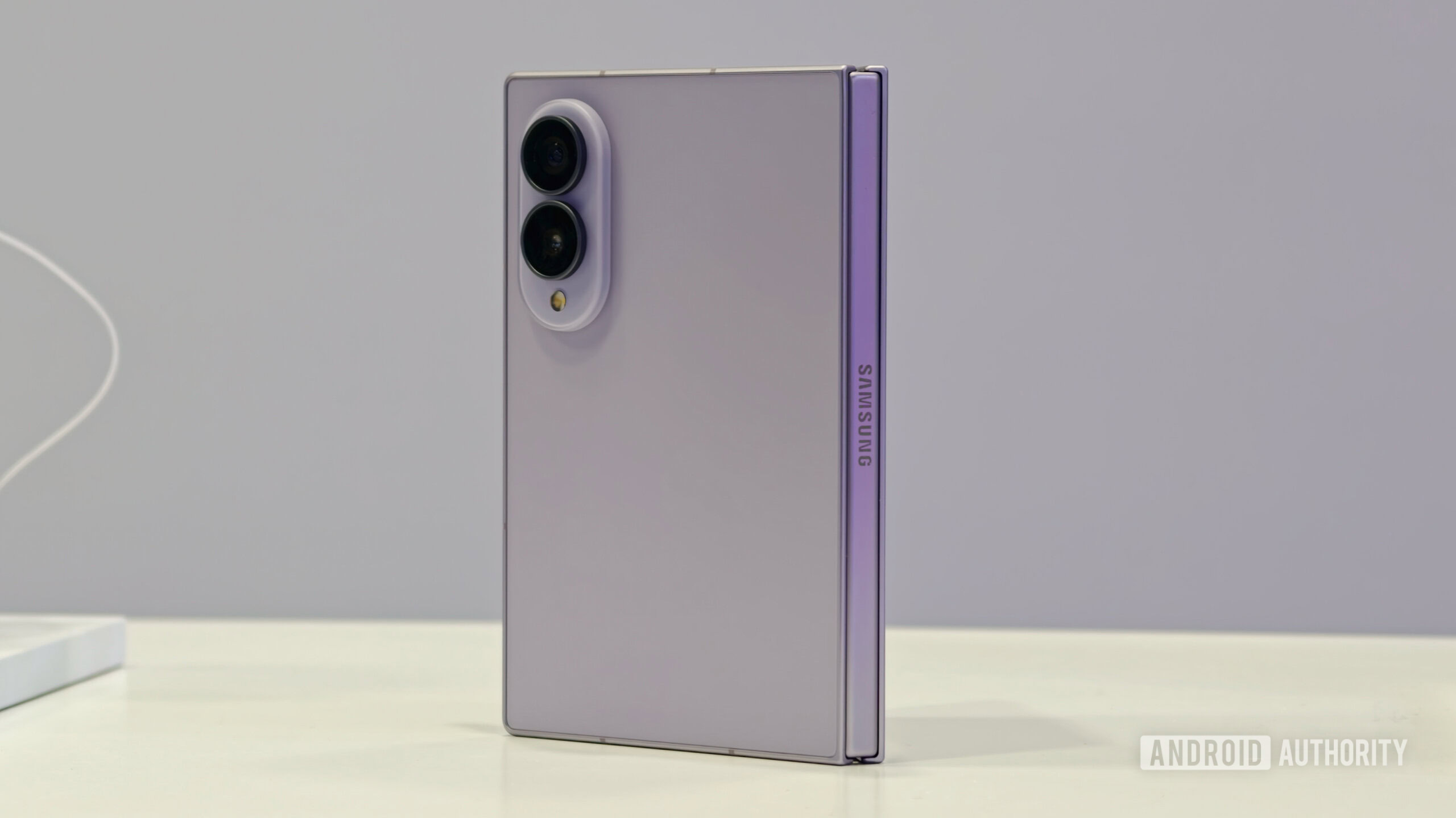 Samsung Galaxy Z Fold 8 in a lavender colorway standing upright on a white table, showing its rear panel, camera module, and engraved Samsung hinge