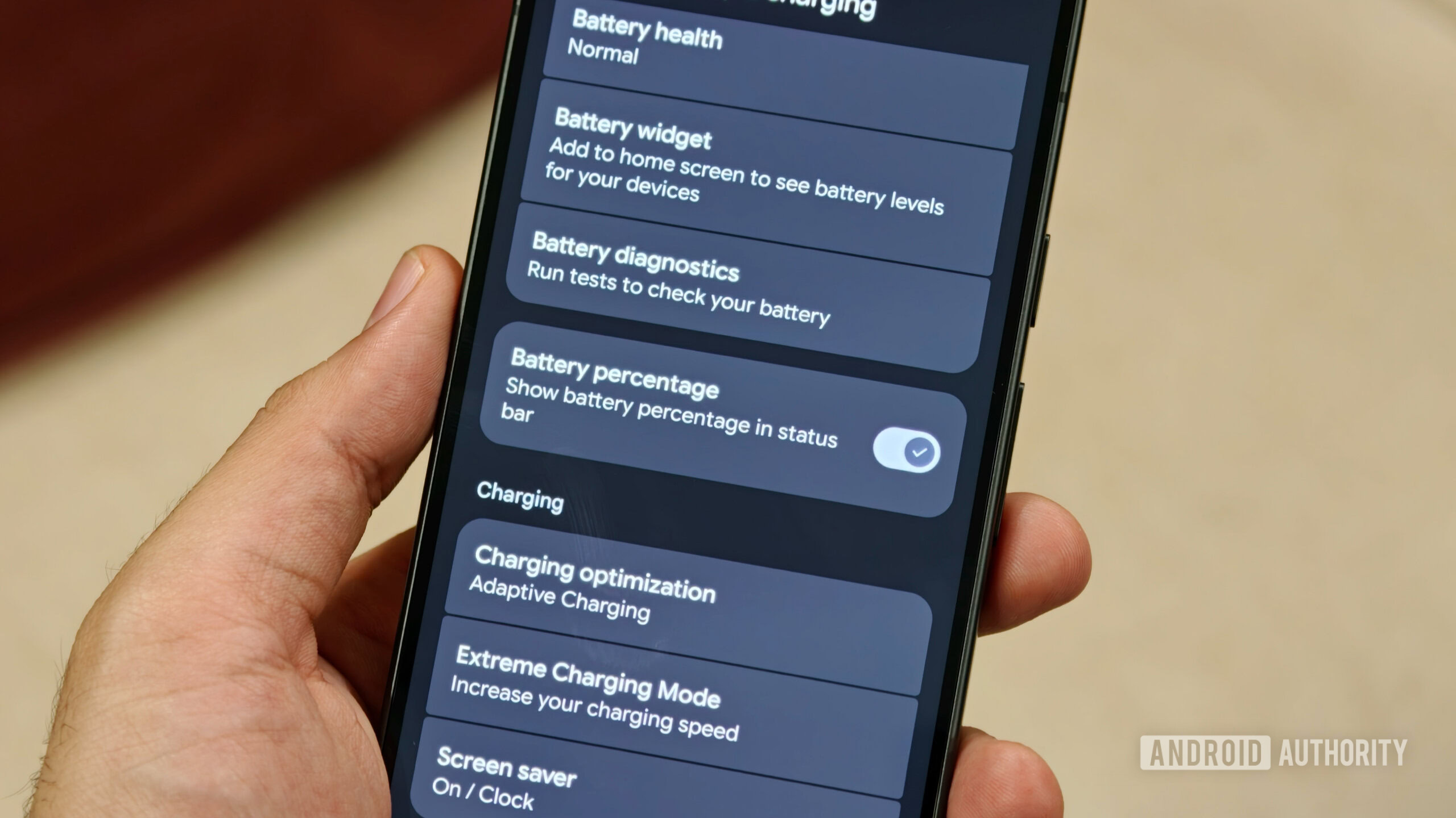 Hand holding Pixel 11 with battery percentage toggle enabled in settings
