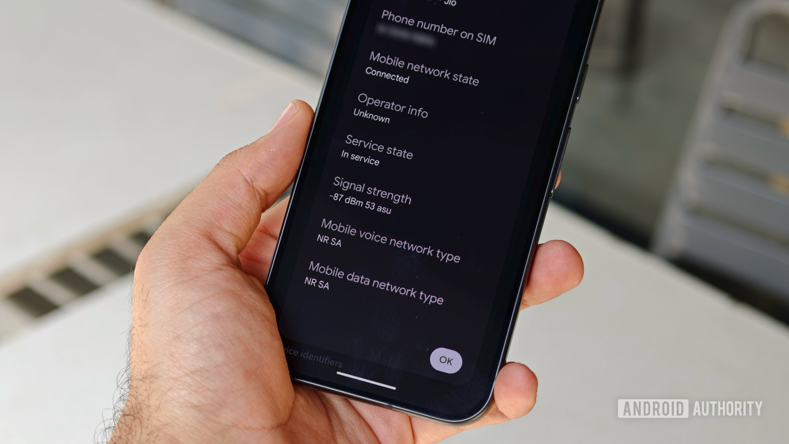 pixel 11 pro vs pixel 10 pro modem 7 A hand holding a Pixel 11 Pro showing Android SIM status settings detailing 5G NR SA network type and signal strength in dBm