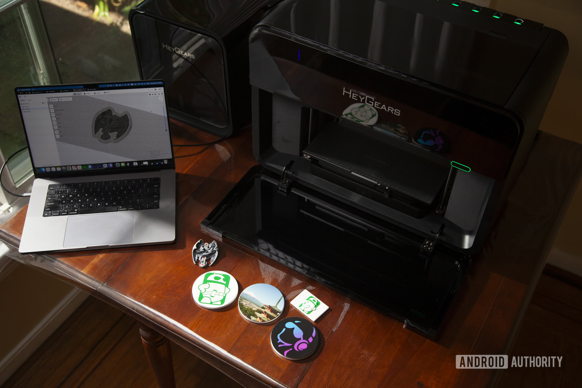 HeyGears G1X full-color 3D printer with macbook and completed full-color 3D model of dragon cross, 2D UV printed designs and photo on coasters, and 3D textured relief design on a fridge magnet