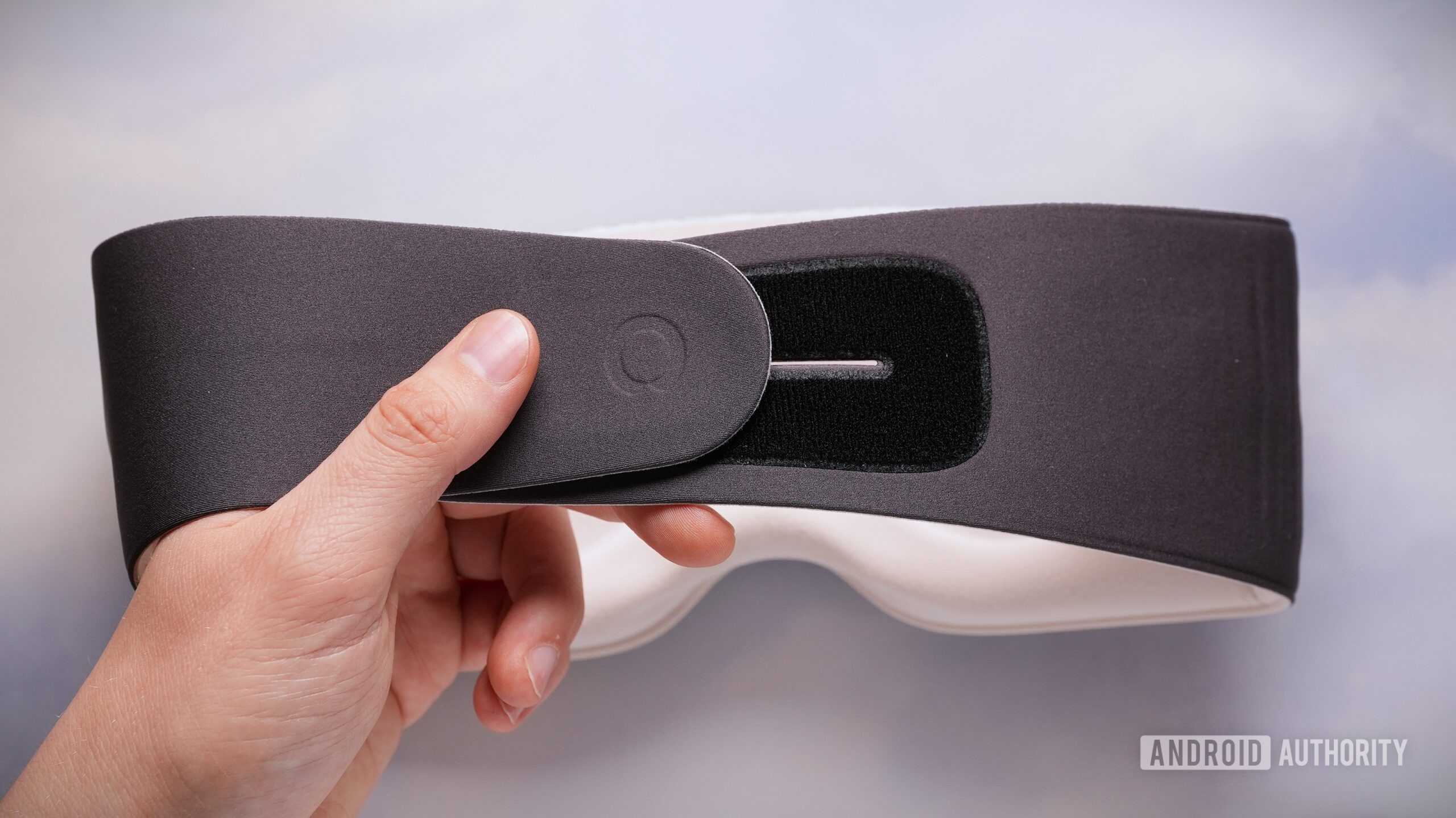 A hand opens the adjustable Velcro strap on the back of the Sleenova sleep mask.