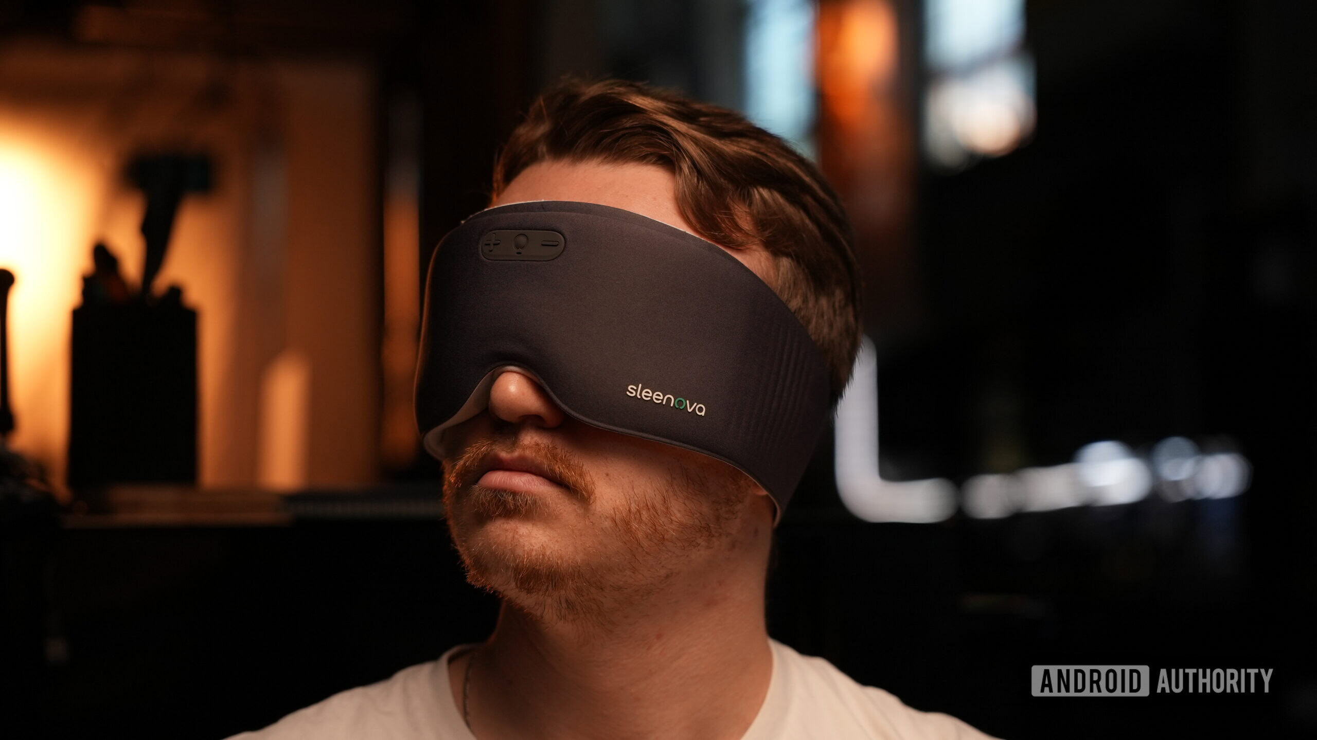 A man wears the gray Sleenova sleep mask, showing its full-coverage design and integrated controls.