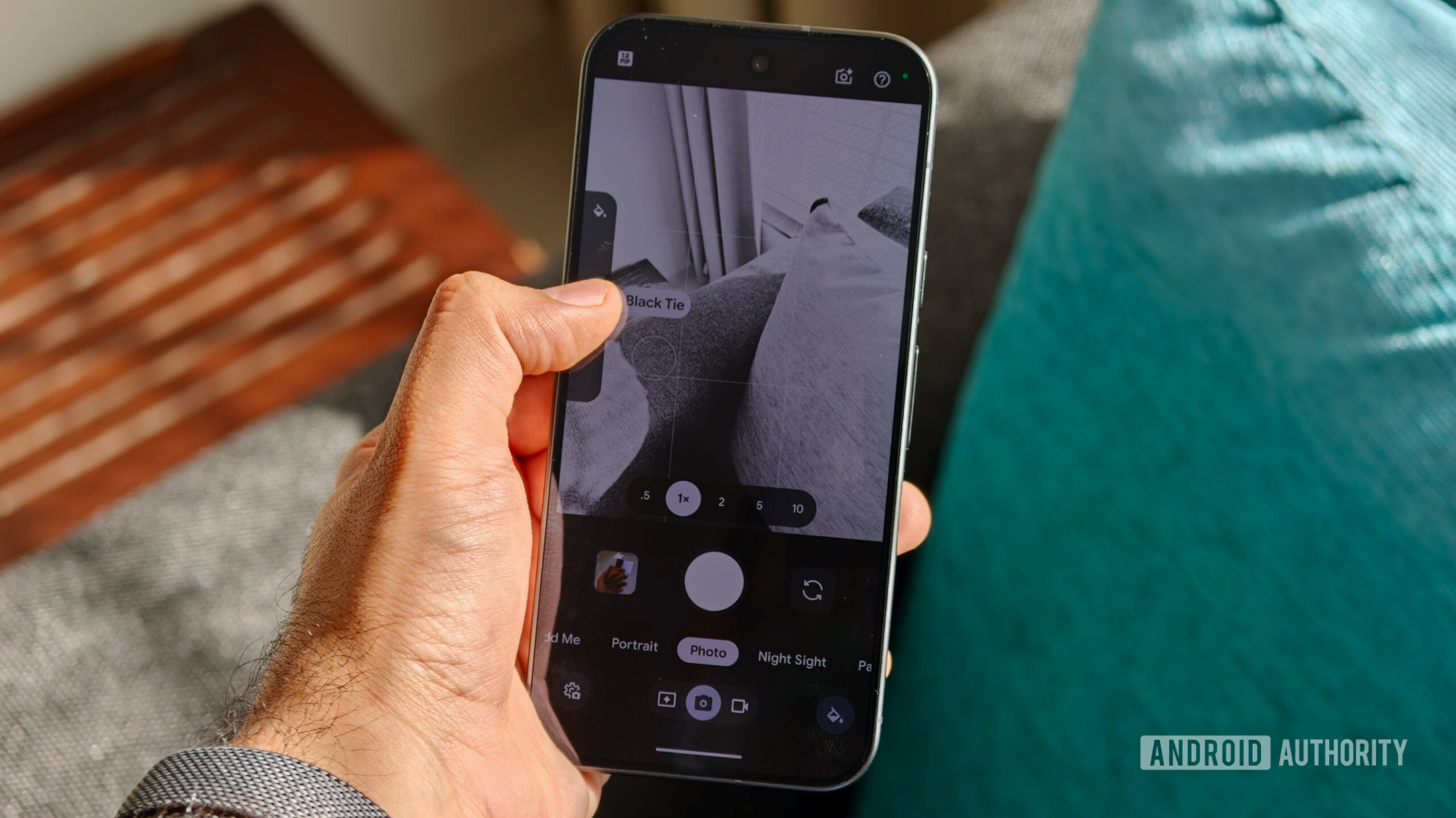 A hand holding a Google Pixel phone with the camera viewfinder displaying a monochrome scene using the "Black Tie" photography Look
